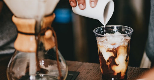 Pouring creamer into an iced coffee.
